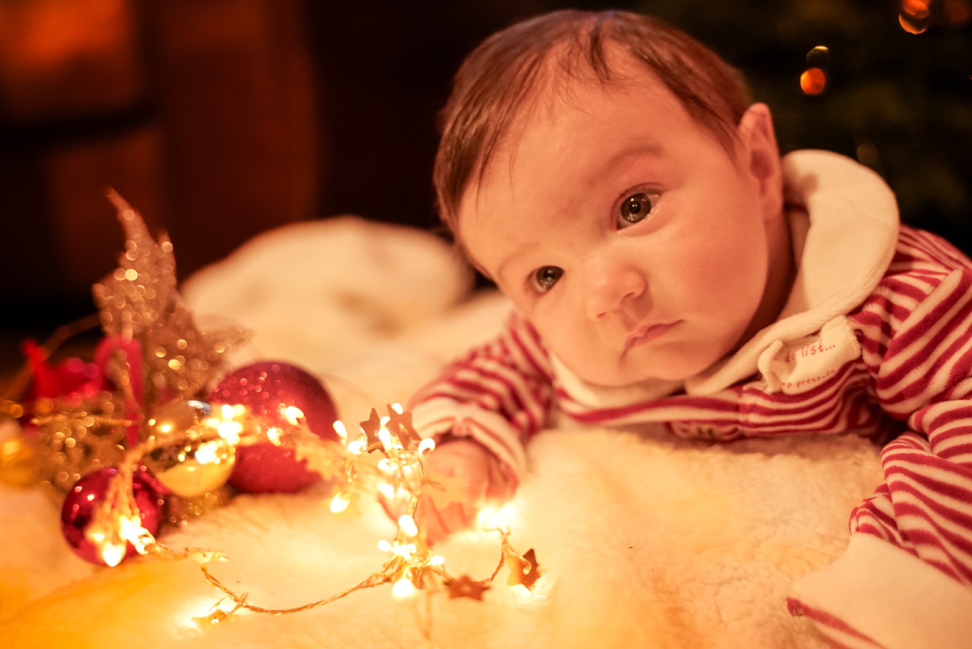 Newborn baby in striped pyjamas beside softly glowing Christmas fairy lights